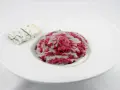 Risotto barbabietola e gorgonzola, un piatto vibrante e saporito, con una fetta di formaggio blu accanto.