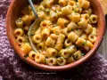 Una ciotola di terracotta piena di pasta e fagioli saporita, con un cucchiaio che ne raccoglie una porzione.