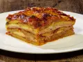Una fetta di parmigiana di patate, stratificata con formaggio e salumi, servita su un piatto bianco.