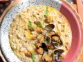 Un cremoso risotto alle vongole, guarnito con prezzemolo tritato e cozze fresche, servito in un piatto bianco a pois.