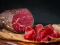 Un pezzo intero e fette sottili di bresaola, con la sua carne rossa e marezzata, evidenziano la differenza tra bresaola e punta d'anca.