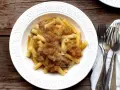 Piatto di pasta con ragù genovese napoletana, servito in un piatto bianco decorato, con forchette d'argento accanto.