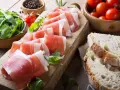 Fette di prosciutto crudo su tagliere con rucola, pomodorini e pane. Scopri come utilizzare il grasso del prosciutto crudo per insaporire i tuoi piatti.