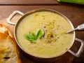 Una ciotola di calda crema di patate, guarnita con erba cipollina e pepe, servita con fette di pane tostato.