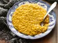 Un cremoso risotto con la zucca, servito su un piatto decorato con un motivo blu e bianco. Un cucchiaio d'argento è immerso nel piatto.