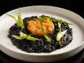 Un piatto di risotto al nero di seppia, guarnito con tartare di salmone e germogli verdi.