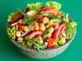 Insalata di ceci colorata con pomodori, cetrioli, cipolla rossa, lattuga e rucola in una ciotola grigia.