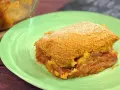 Una fetta di pitta di patate dorata e croccante, con un ripieno succulento di patate e pomodoro, servita su un piatto verde.