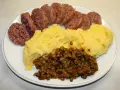Piatto con fette di cotechino o musetto, polenta gialla e lenticchie stufate.