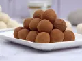 Montagna di tartufi al cioccolato senza panna, spolverati di cacao, su un piatto bianco. Sullo sfondo, altri dolcetti chiari.