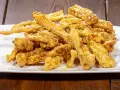 Un mucchio di croccante trippa fritta dorata, cosparsa di scorza di limone, su un piatto bianco.