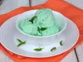 Coppa di cremoso gelato alla menta con latte condensato, guarnito con foglie di menta fresca.