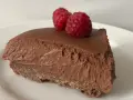 Una fetta di torta mousse al cioccolato, soffice e golosa, guarnita con due lamponi freschi su un piatto bianco.