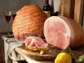 Due prosciutti, uno intero e uno affettato su pane, con una bottiglia di vino e un limone. Il cotto prosciutto è pronto per essere gustato.