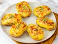 Patate ripiene al forno, dorate e gratinate, guarnite con rosmarino fresco. Un piatto invitante e saporito.