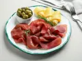 Bresaola con formaggio da abbinare, olive verdi e rosmarino su un piatto.