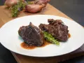 Guancia di manzo brasata, tenera e succulenta, servita su un piatto bianco con rosmarino fresco. Un piatto che fa chiedere: guancia di manzo cos'è?