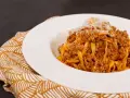 Tagliatelle ricche con sugo finto e parmigiano grattugiato, servite su un piatto bianco con tovagliolo decorato.