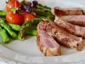 Fette di manzo magro cos'è? Succulenta carne con asparagi verdi e pomodorini su un piatto bianco.