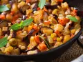 Caponata ricetta: melanzane, carote, olive e pinoli in padella, guarnita con basilico fresco. Un piatto colorato e saporito.