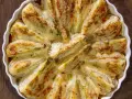Finocchi al forno dorati e gratinati, serviti in una pirofila bianca su un tavolo di legno scuro.