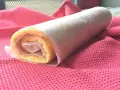 Rotolo di torta biscotto appena preparato, avvolto in carta forno, adagiato su un panno rosa.