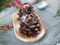 Deliziose pigne dolci decorate con zucchero a velo, su un vassoio di legno, con rami di pino e bacche rosse sullo sfondo.