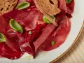 Fette di bresaola e barbabietola, esempi di salumi non insaccati quali sono, con crostini e basilico.