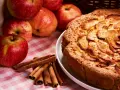 Torta mele, noci e cannella dorata, con mele fresche e bastoncini di cannella su una tovaglia a quadri rosa.