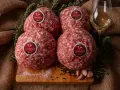 Quattro sfere di carne macinata TASTASAL, con rosmarino, aglio, pepe e sale su un tagliere. Ingredienti freschi per un sapore autentico.