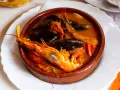 Una ricca zuppa di pesce in ciotola di terracotta, con gamberoni, cozze e pomodorini.