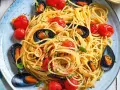 Un piatto invitante di spaghetti con le cozze e pomodorini, condito con prezzemolo fresco e pepe nero.