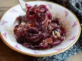 Un cucchiaio solleva un mucchietto di cipolle caramellate, lucide e invitanti, in una ciotola decorata.