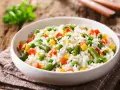 Un piatto di riso per insalata di riso, con piselli, carote, fagiolini e mais, su un tovagliolo di stoffa marrone.
