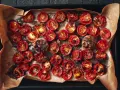 Pomodori al forno, caramellati e succosi, con aglio arrostito e rosmarino su carta forno.