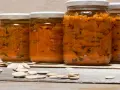 Barattoli di zucca sott'olio in agrodolce, con semi di zucca sparsi sul tavolo di legno.