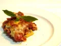 Porzione di pasta ncasciata fumante, con formaggio filante e basilico fresco, su un piatto bianco.