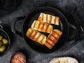 Quattro fette di galbanino alla piastra dorate e striate, servite in una padella di ghisa, con olive e sale rosa a lato.