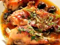 Coniglio alla ligure succulento, con olive nere e erbe aromatiche, immerso in un sugo dorato.