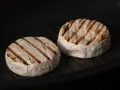 Due forme di formaggio da fare alla piastra, con belle striature dorate, cuociono in una padella scura.
