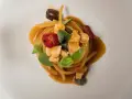 Un piatto di pasta con il pesce, condita con pomodorini, olive, capperi e basilico, servita su un piatto bianco.
