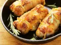 Involtini di pollo al forno dorati e succulenti, legati con spago da cucina e guarniti con rametti di rosmarino fresco, serviti in una padella di ghisa.