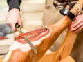 Mani esperte dimostrano come tagliare il prosciutto crudo con un coltello affilato, creando fette sottili e gustose.