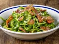 Un piatto invitante di pasta con spinaci, condita con croccante pancetta e parmigiano grattugiato, servita in una ciotola bianca con bordo blu.