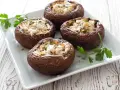 Quattro funghi ripieni al forno, dorati e invitanti, guarniti con prezzemolo fresco su un piatto bianco.