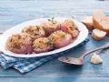 Deliziose cipolle al forno, dorate e profumate, servite su un piatto bianco con pane croccante e un cucchiaio d'argento.