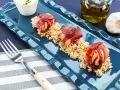 Tre bocconcini di pollo con pancetta avvolti e dorati, serviti su un letto di riso integrale.