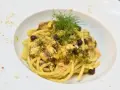 Un piatto invitante di pasta con finocchi, olive e acciughe, guarnito con erbe fresche e pangrattato.