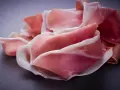 Fette di prosciutto crudo, un insaccato dal colore rosato e venature bianche, disposte su una superficie scura.