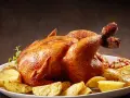 Un succulento pollo allo spiedo dorato, servito con patate arrosto e aglio su un piatto bianco.